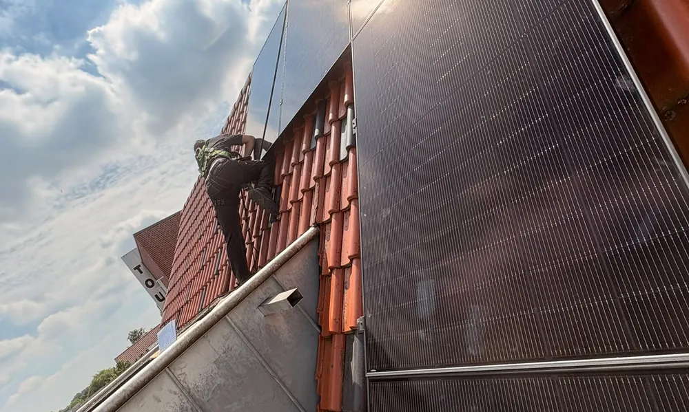 Monteur met valbeveiliging plaatst zwarte zonnepanelen op een dak met rode dakpannen