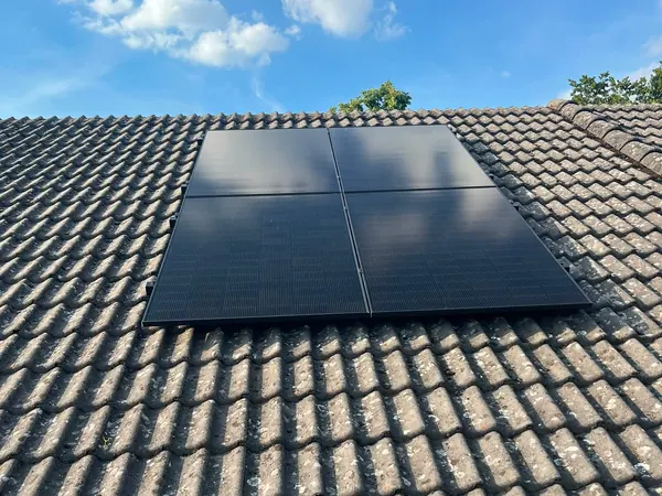 Vier zwarte zonnepanelen op een dak met grijze betonpannen