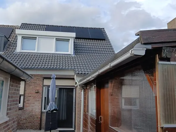 Achterkant van een woning met zwarte zonnepanelen naast de dakkapel