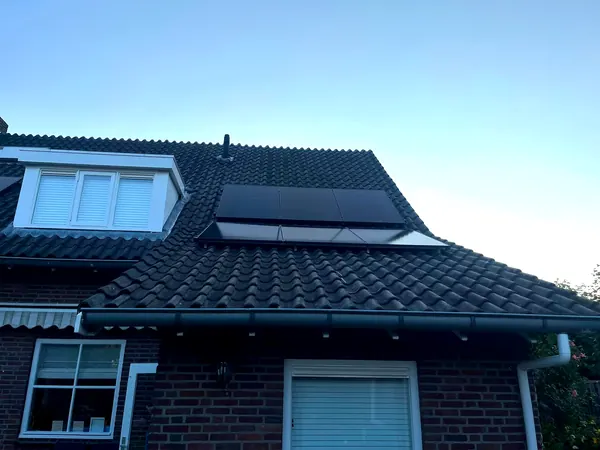 Twee rijen zwarte zonnepanelen op een donker pannendak naast een dakkapel