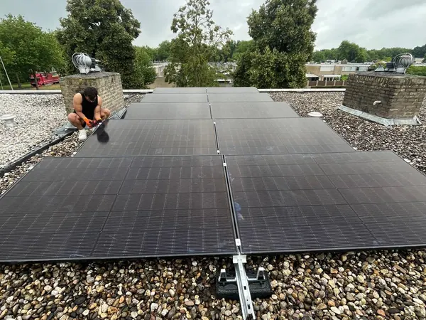 Monteur sluit zwarte zonnepanelen aan op een plat dak met grind
