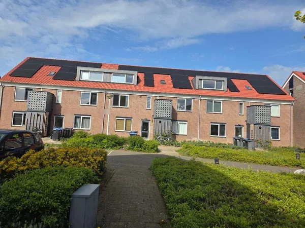 Rij woningen met zwarte zonnepanelen op rode pannendaken onder een blauwe lucht