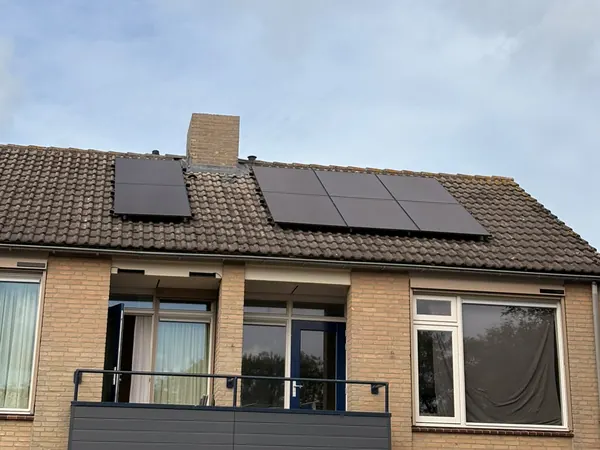 Woning met balkon en zwarte zonnepanelen aan beide kanten van de schoorsteen