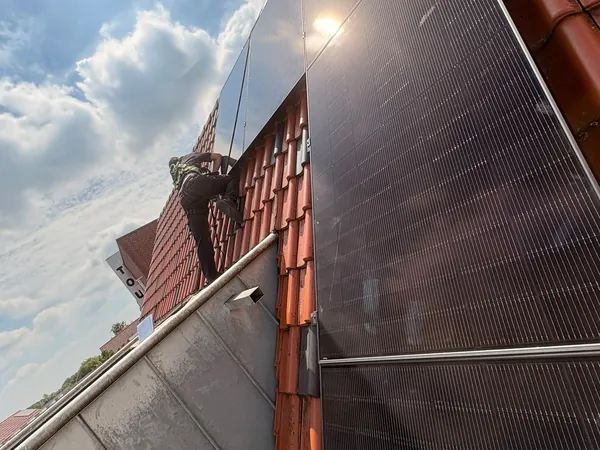 Monteur met valbeveiliging plaatst zwarte zonnepanelen op een dak met rode dakpannen