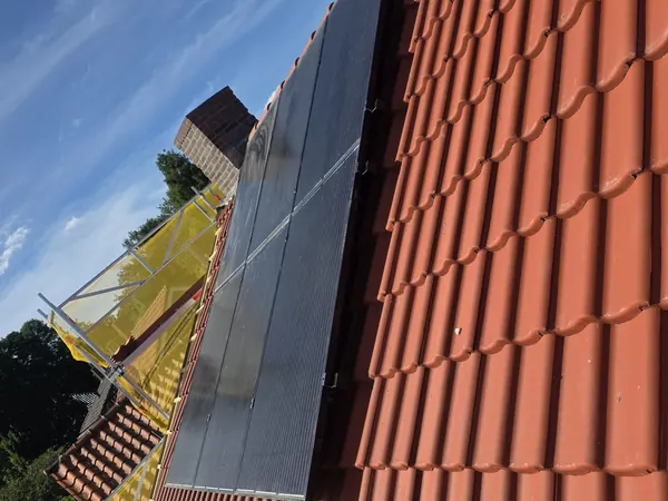 Zwarte zonnepanelen op een rood pannendak met een steiger ernaast